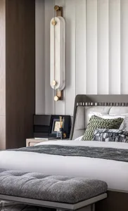 Modern bedroom featuring a bed with upholstered headboard and green throw pillows, accented by a marble sconce and a textured