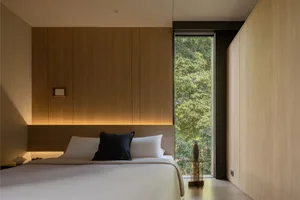 A modern bedroom featuring wooden paneling, a large window, and a bed with white sheets and black accent pillow.