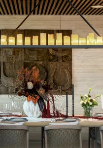 Modern dining room with marble and glass table, fabric chairs, wooden ceiling accents, and a decorative centerpiece.
