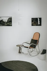 A minimalist living room featuring a metal rocking chair with a green cushion and a round rug on a white floor.