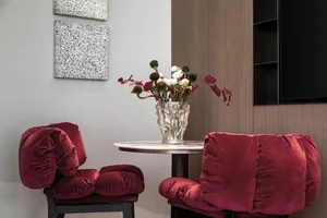 A modern living room with a marble-top table and two plush red velvet chairs.