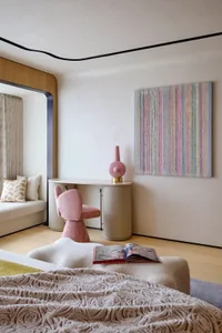 A modern minimalist bedroom featuring textured fabrics, a pink chair, a colorful abstract painting, and a cozy atmosphere.