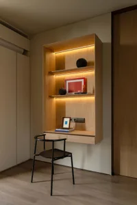 A modern study corner featuring a floating shelf with built-in lighting, black chair, and decorative items.