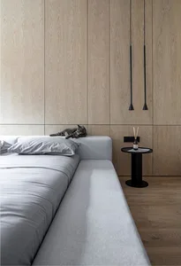 A serene modern bedroom featuring a gray upholstered bed with light wood paneling on the walls and a small side table.