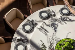 Modern dining room featuring a round marble table with glass and metal accents, set with elegant tableware and floral decorat