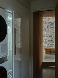Modern laundry room featuring concrete and stone walls, wooden cabinets, and a white appliance.