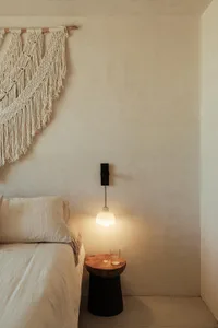 A minimalist bedroom with a concrete side table, textured plaster walls, and a macramé wall hanging.
