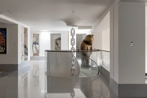 A minimalist interior space featuring a glass railing with a bronze bear statue.