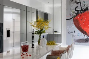 A modern kitchen featuring white marble countertops and cabinets, adorned with yellow flowers in a glass vase, and a white an