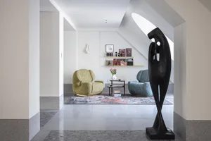 A modern living room with a concrete rug, green armchair, and black sculpture.