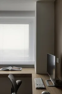 A minimalist home office setup featuring a wooden desk, a sleek computer monitor, a keyboard, and a chair.