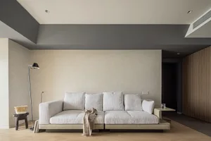 A minimalist living room featuring a beige sofa with white cushions, a wooden floor, and a floor lamp.