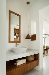 Modern minimalist bathroom with a white marble sink, wooden shelves, and a wooden pendant light.
