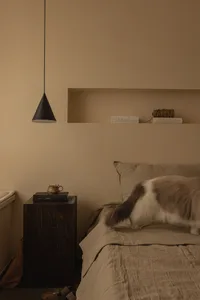 A minimalist bedroom featuring fabric bedding, wooden furniture, and metal accents on a bed with a window and a black pendant