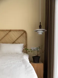 A minimalist bedroom with a wooden headboard, white bedding, and a potted plant on a wooden nightstand.