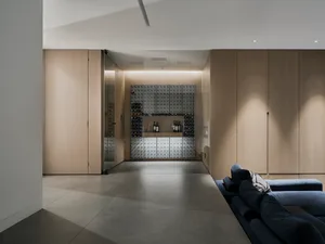 A minimalist living room featuring polished concrete flooring, wooden furniture, and glass walls.