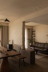 A minimalist living room with neutral tones and wooden elements, featuring a stone column and floating shelves.