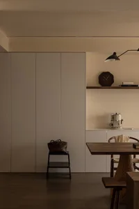 A minimalist kitchen with white-painted board cabinetry and a wooden table with chairs.