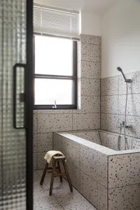 Modern bathroom interior with terrazzo tiles, a window, a bathtub, and a stool.