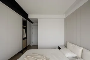 A minimalist bedroom with white and grey walls, a neatly made bed, and hidden storage cabinets.
