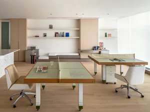 A modern home office space featuring a wooden table and chairs, with books and magazines on shelves in the background.