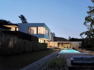 Modern house with glass walls at night, featuring wood and concrete exterior.