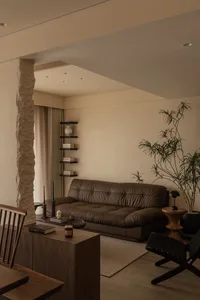 A modern living room featuring a dark leather sofa and wooden furniture, with a minimalist design and warm tones.
