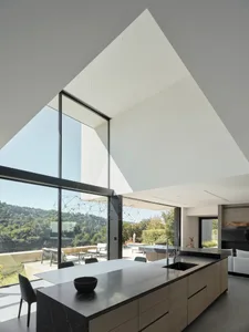 Modern kitchen with glass cabinets, open layout, and floor-to-ceiling windows overlooking greenery.