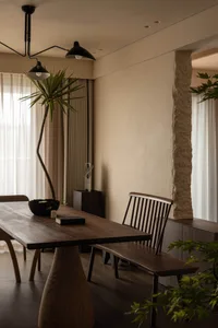 A minimalist dining room with a wooden table, stone pillars, and modern lighting fixtures.