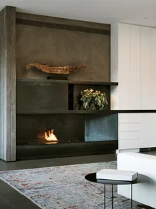 Minimalist living room with concrete fireplace and white furniture, featuring a floral arrangement on the mantel.