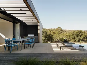 Modern outdoor space with sustainable concrete design, featuring dining area and lounge chairs surrounded by nature.