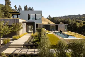 A modern residential house with a metal frame, large glass windows, and wood accents.