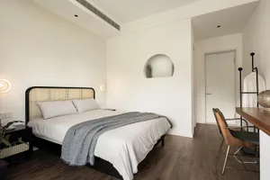 Modern minimalist bedroom with a white bed, grey throw blanket, and wooden floor.