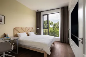A minimalist bedroom featuring wooden furnishings, white bedding, and large windows.