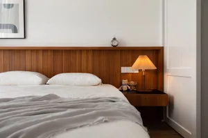 A modern minimalist bedroom with a wooden bed frame and a wooden headboard. The room features a soft, white bedspread and a w
