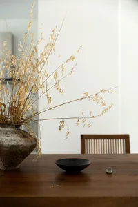 A minimalist dining room featuring wooden furniture and dried grasses in a vase on a wooden table.