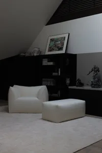 A modern living room with a white leather armchair and footstool, black furniture and decor, and minimalist design.