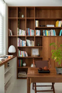 A cozy home office featuring a wooden desk, chairs, and shelves filled with books and decorative items.