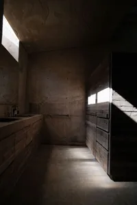 Modern bathroom with concrete walls and floor, featuring a minimalist design and natural light from a window.