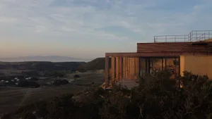 Modern house with wooden exterior and large glass windows overlooking the valley.