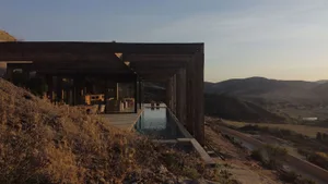 Modern minimalist house with wood and concrete exterior materials, featuring a long pool and scenic landscape view.