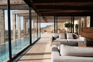 A modern residential lounge area with concrete flooring and large glass walls overlooking a pool.