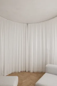 A minimalist living room with white curtains and wooden flooring.
