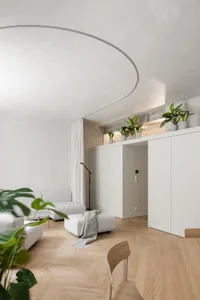 A modern living room with white furniture, wooden flooring, and green plants.