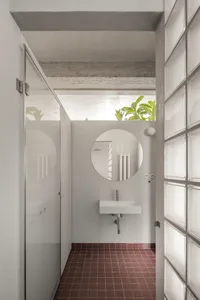 Modern minimalist bathroom featuring a glass shower enclosure, concrete floor, and a circular mirror above a wall-mounted sin