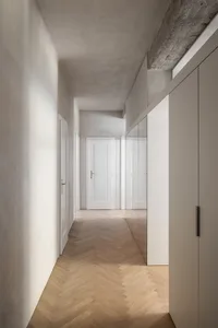 A modern interior corridor featuring wooden flooring, concrete walls, and metal accents.