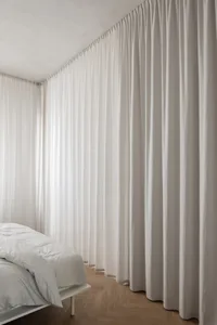 A minimalist bedroom featuring white curtains made of textured canvas material, creating a serene and elegant atmosphere.