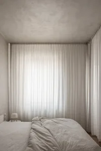 Minimalist bedroom featuring a bed with white sheets and curtains.