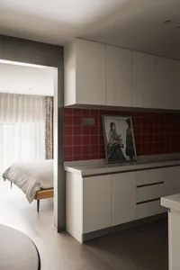 A minimalist kitchen with red tiles and white cabinets.