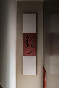 A modern-style calligraphy scroll with a red background and black text hanging on a light-colored wall.